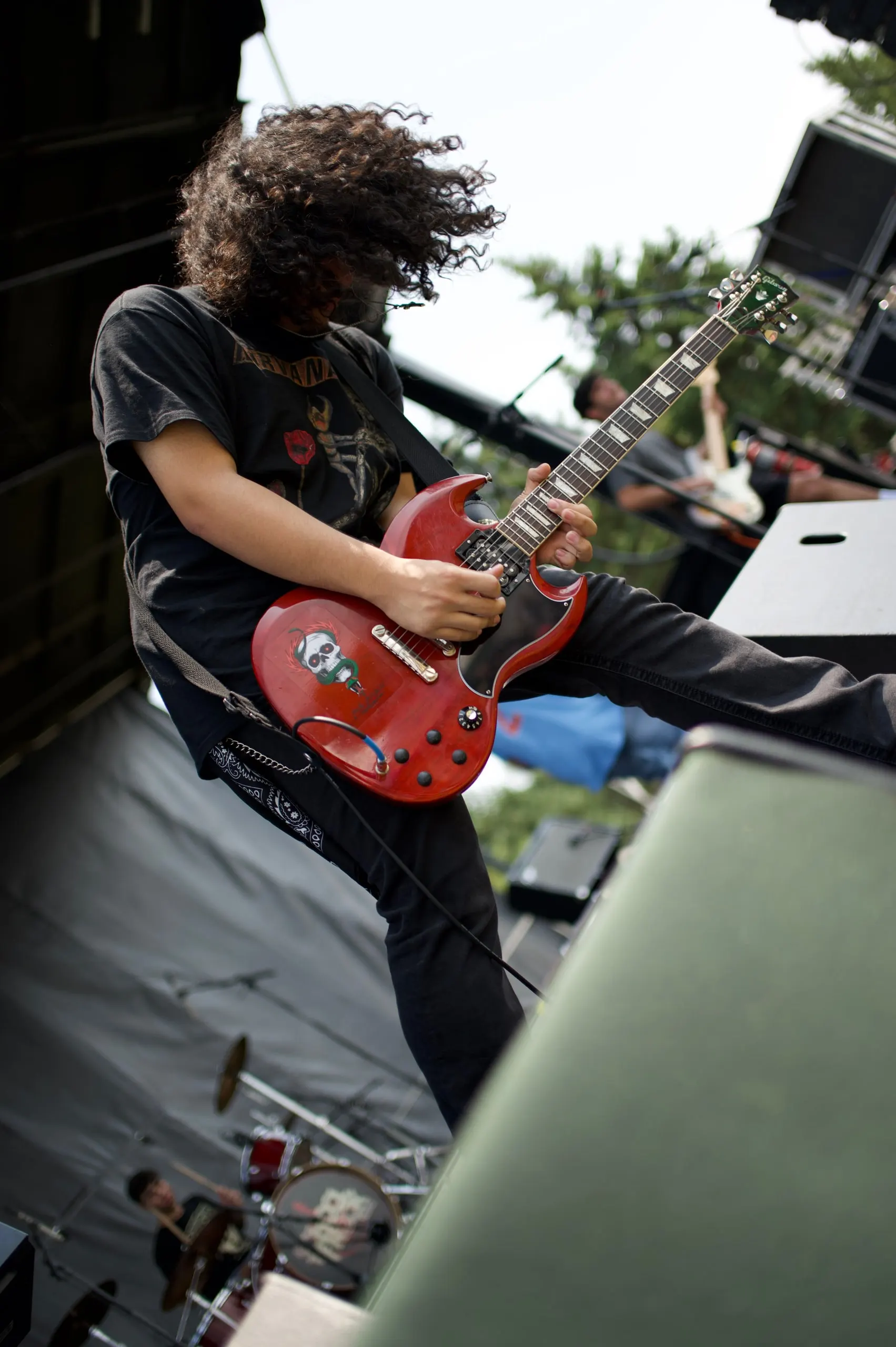 A guitarist mid-solo on stage, hair flying, with a red electric guitar