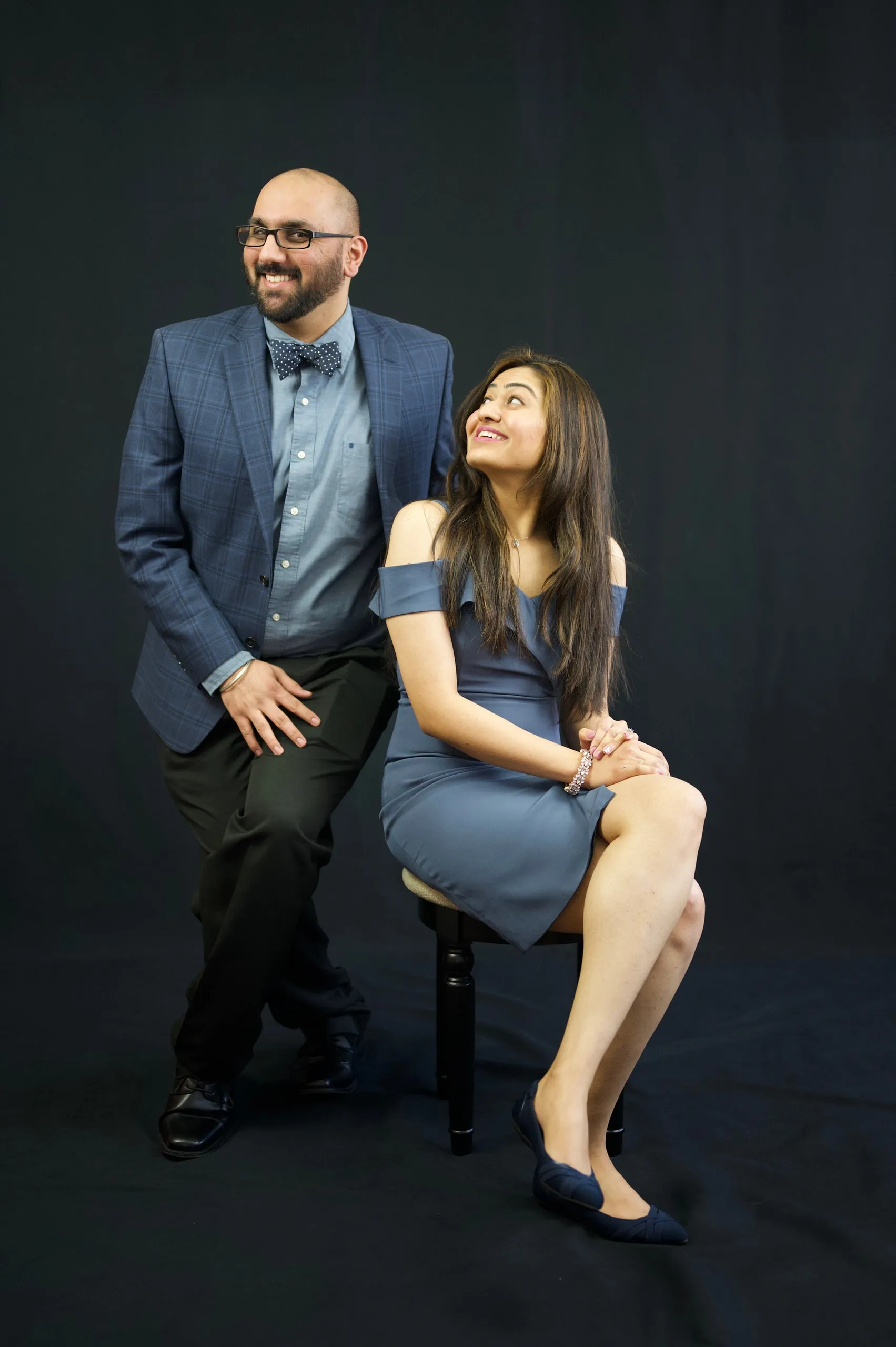 A smiling couple in formal wear posing together in a studio against a dark backdrop