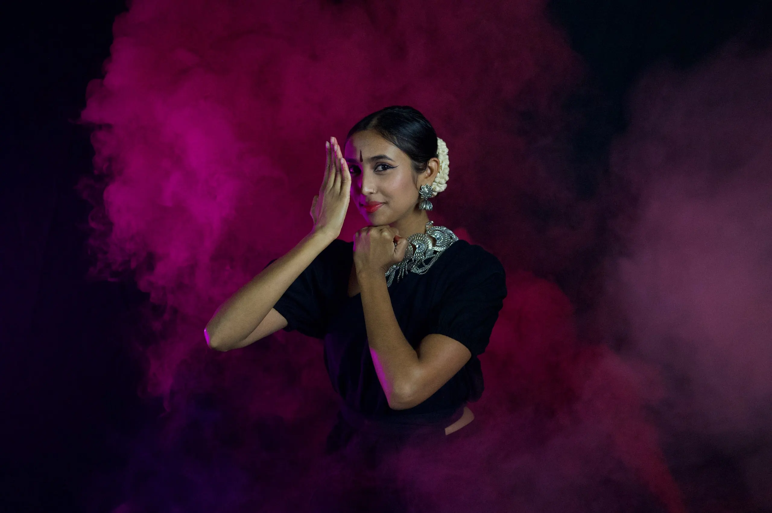 A woman posing with one hand raised, surrounded by magenta smoke
