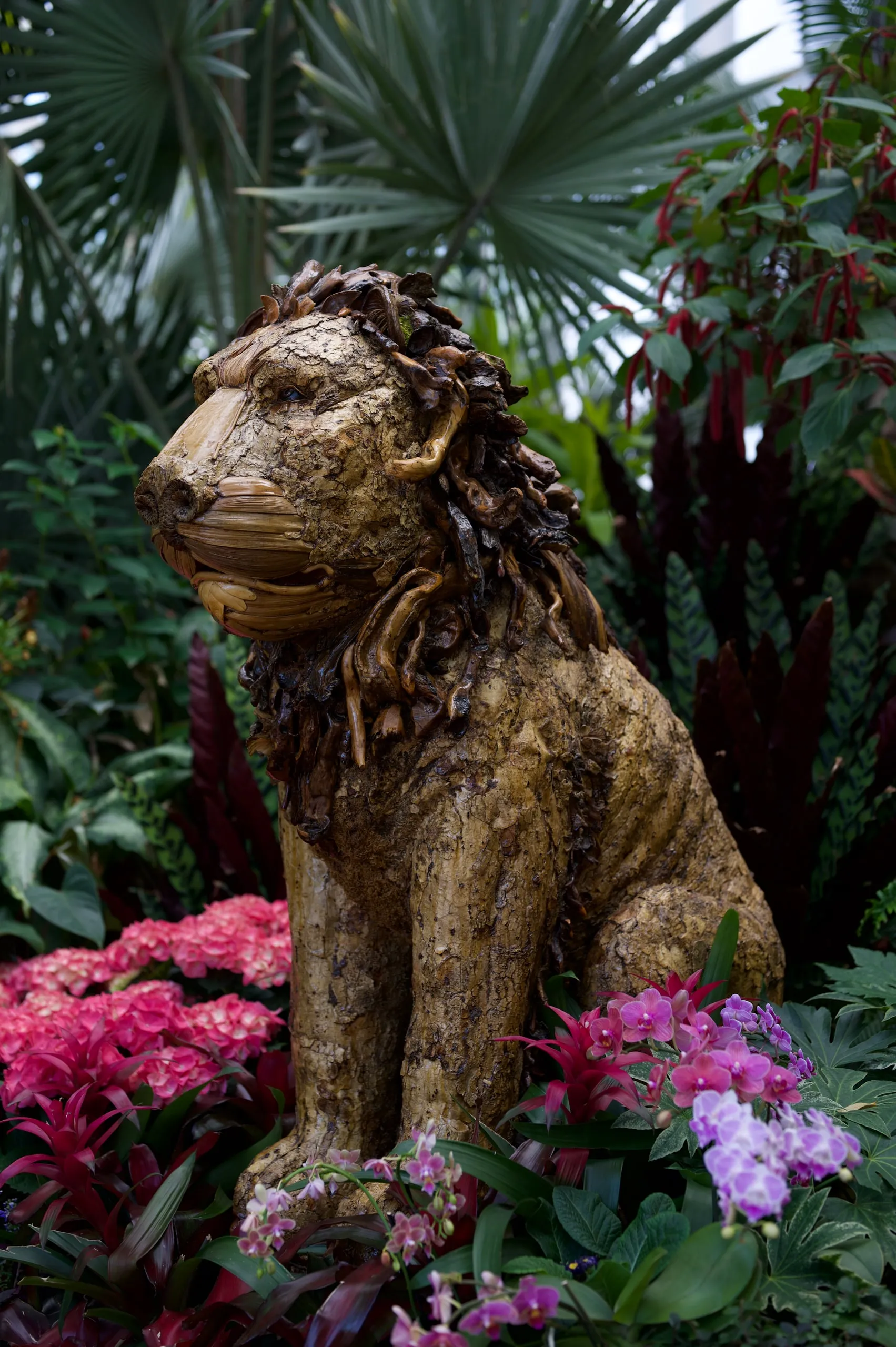A carved wooden lion sculpture surrounded by pink flowers and palm fronds